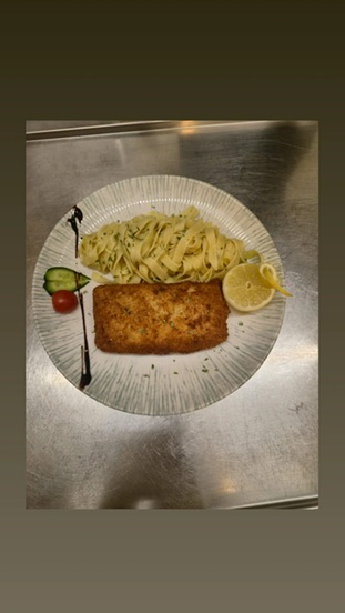 Paniertes Gericht mit Pasta und Zitrone auf einem weissen Teller